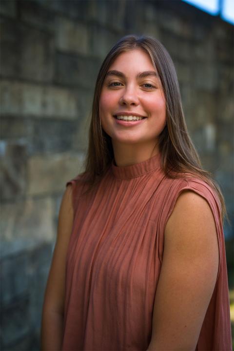 Master of Science in Nutrition student Lucy Ward. Lucy has tanned white skin. She has brown hair that drapes down her back. She wears a rust-colored top.