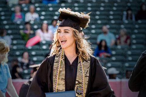 A woman in a grad cap and gown wearing a camouflage stole smiles