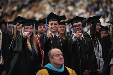 Three graduates point toward the camera at commencement