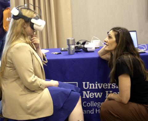 A young woman uses a virtual reality headset while a woman talks with her.