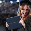 A female graduate smiles while displaying her diploma after walking across the stage