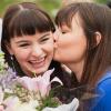 A graduate holding flowers smiles while getting a kiss on the cheek from another woman
