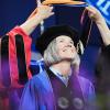 A woman graduate looks up as a commencement hood is placed over her shoulders