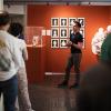 A man in front of an orange wall speaks to a small standing crowd